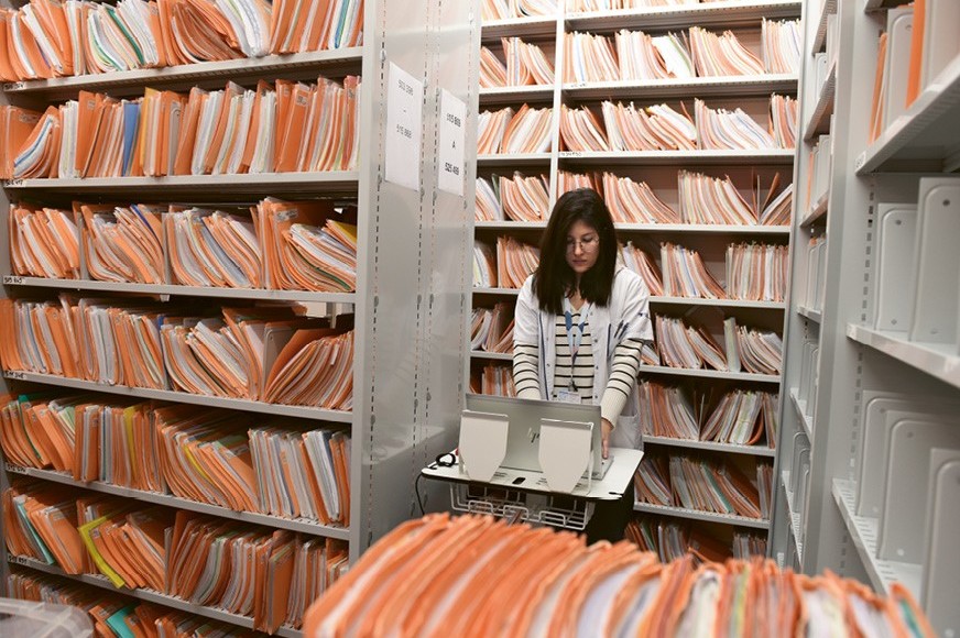 Photo d'une collaboratrice dans les archives de l'Hôpital, contenant les dossiers des patients.