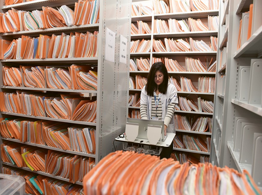 Photo d'une collaboratrice dans les archives de l'Hôpital, contenant les dossiers des patients.