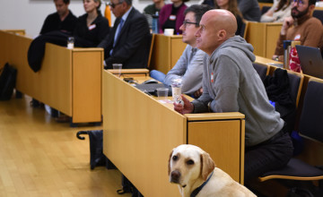 Image des participants au "Symposium sur l’accessibilité dans les milieux de formation", avec un chien guide en premier plan pour l'article Inclure