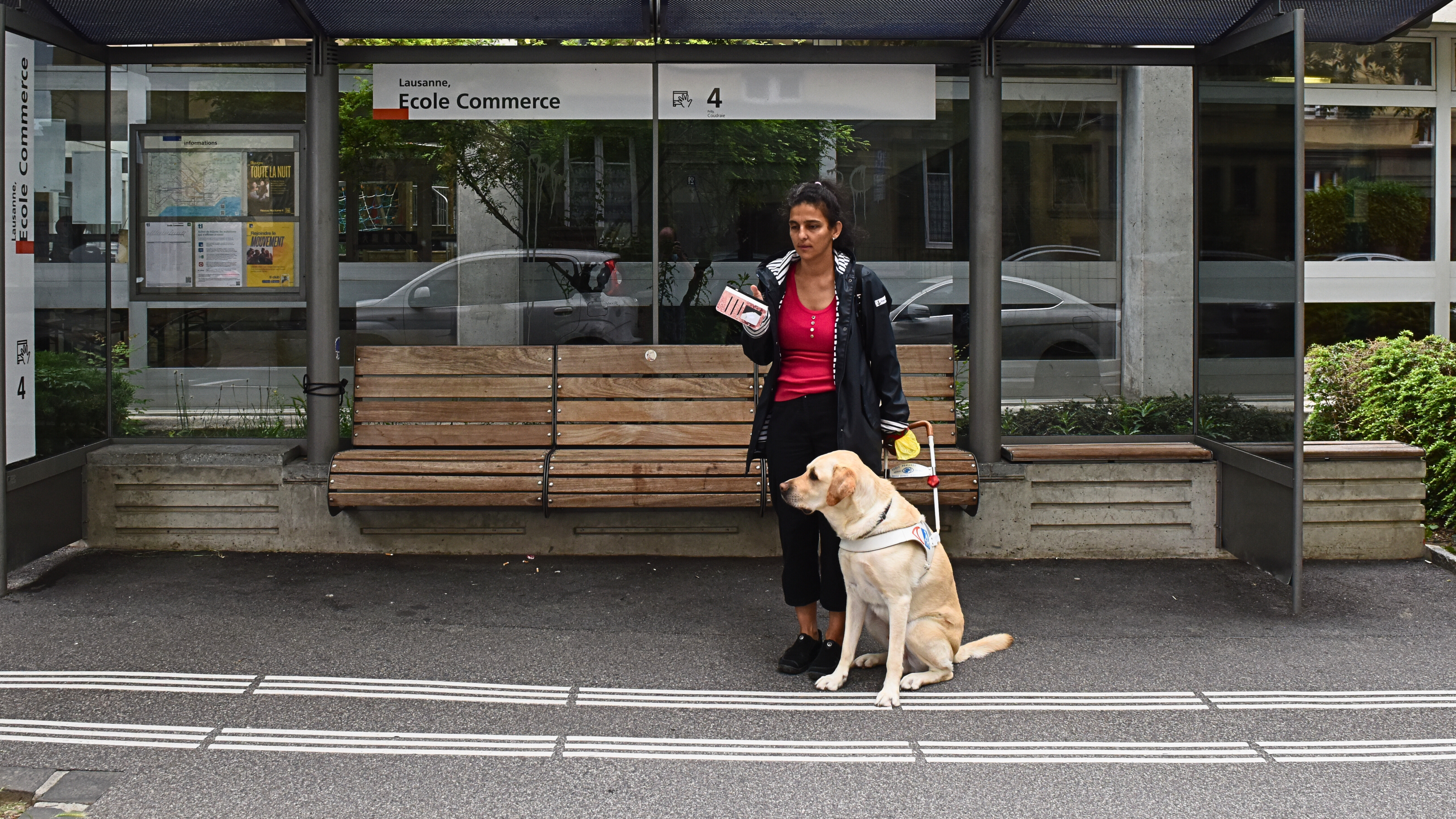 Rania, malvoyante, attendant à un arrêt de bus avec son chien guide